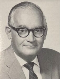 A photo of a man wearing glasses and a suit.