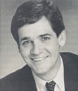 A middle-aged man in a suit smiles.
