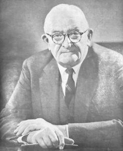 An older man wearing glasses and a three-piece suit.