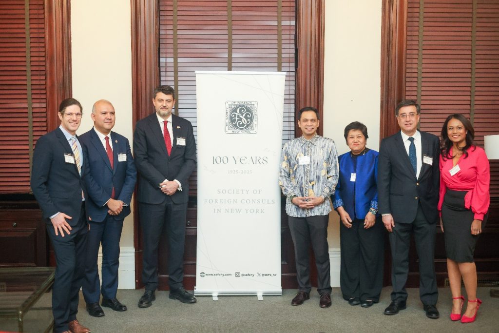 Five men and two women in Western-style business attire, in a few cases with Malay and Thai touches, pose with a banner that reads, "100 Years: 1925-2025: Society of Foreign Consuls in New York."