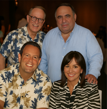 Four people in professional dress or Hawaiian shirts pose for a photo, with two men standing and a woman and a man seated.