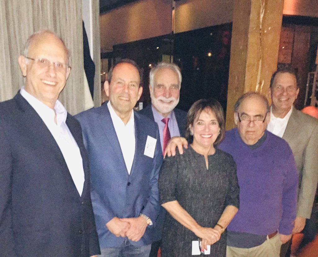 One woman and five men pose, smiling broadly.